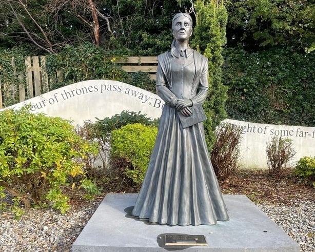 A life-sized stone statue of Frances Browne, situated on a flat stone plinth, surrounded by greenery.