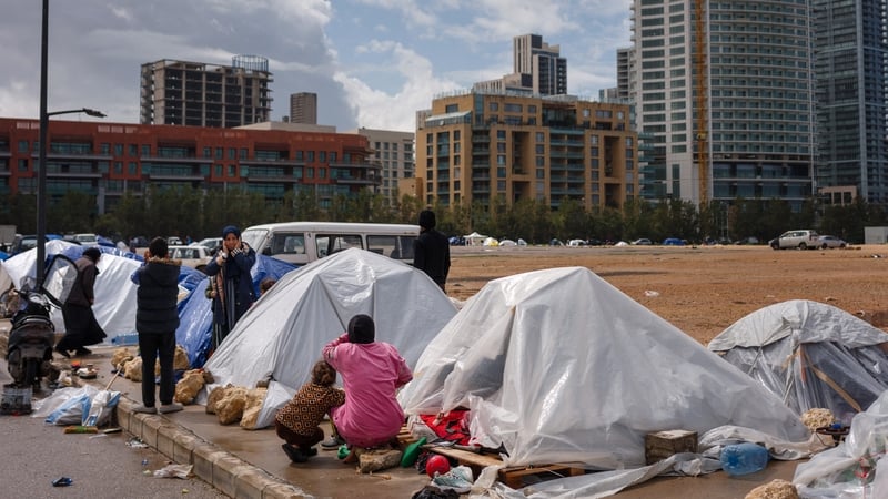 Displaced families stand next to their tents covered with plastic sheets as they react to an Israeli warplane flying over Beirut on March 20, 2026. Lebanon was drawn into the Middle East war on March 2, when militant group Hezbollah launched rockets towar