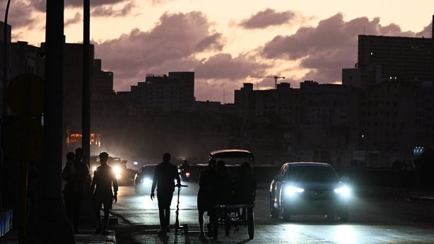 people are seen alongside moving vehicles in a darkened street during a blackout