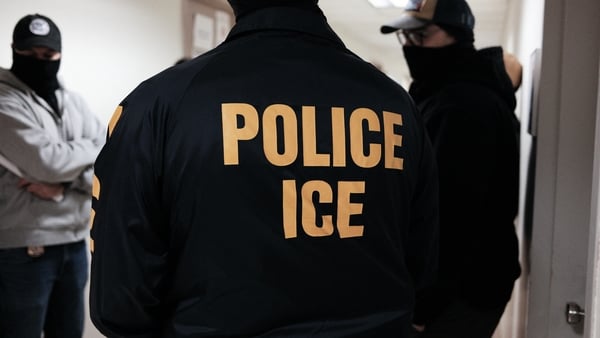 Masked federal agents wearing a Police ICE jacket