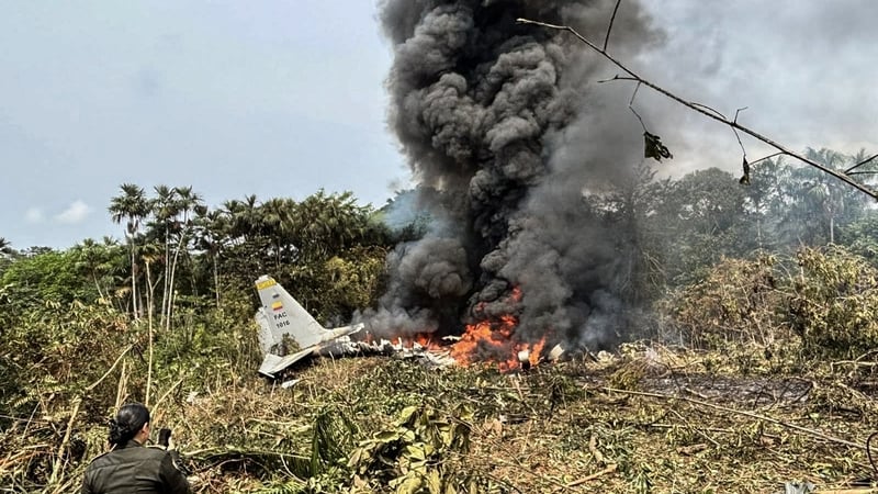 Flames and thick black smoke rise from an Air Force Hercules that crashed during takeoff, as a member of the Colombian Police stands nearby