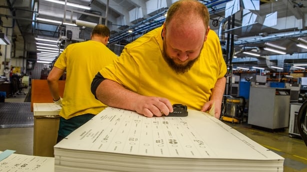 a man leans over a stack of printed paper