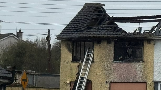 image shows a badly burned out house with a ladder leaning against it