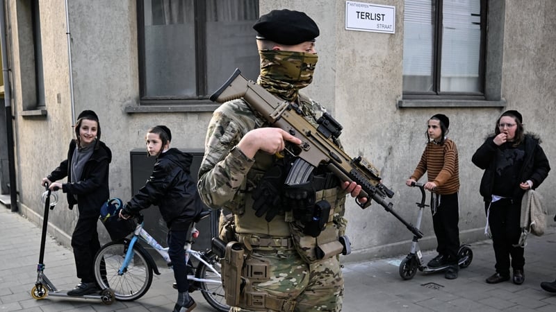 Members of the Jewish community walk past Belgian military personnel armed with FN SCAR assault rifles standing guard in central Antwerp