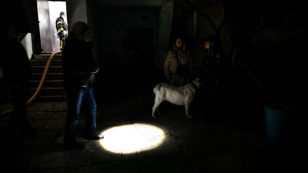 Light from a torch is seen as people and a dog stand in the darkness 