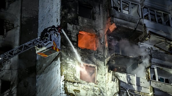 A firefighter on a latter sprays water from a hose onto a fire in a building which shows extensive damage