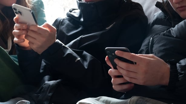 two teenagers look at screens displaying various social media and messaging apps 