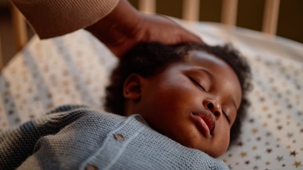 Close up on peaceful face of Black baby girl sleeping in crib while mothers hand gently caressing kids hair in childrens bedroom
