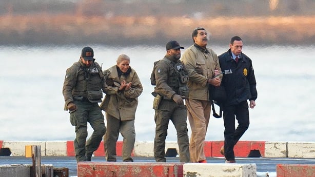 This photograph shows a man and woman, both in handcuffs, being escorted by three law enforcement officers