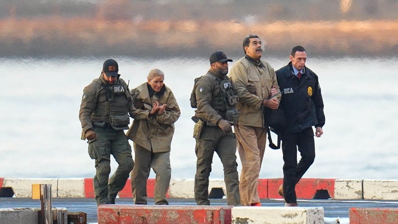 This photograph shows a man and woman, both in handcuffs, being escorted by three law enforcement officers