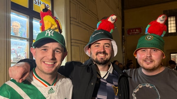 three men smile for the camera as they wear bucket hats with toy parrots stuck on them