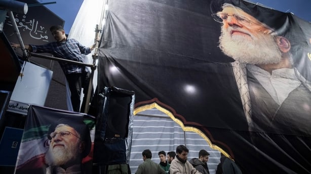 a group of men are seen standing beneath a huge banner depiciting an older man with a beard