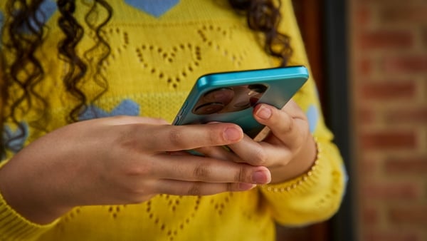 A teenager in a yellow jumper holds a mobile phne in her hands
