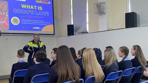 Children in school uniforms listen as a garda in uniform speaks to them
