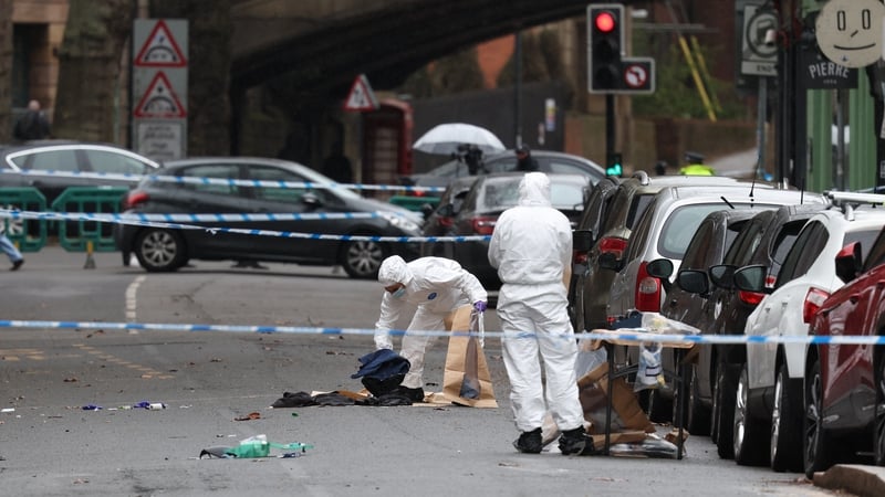 Police forensic officers fill evidence bags while working amongst a variety of personal items seen covering the road