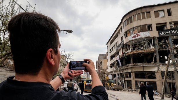 A man films with a phone from the street the destruction on an office building that housed the offices of the Doha-headquartered news network Al Araby TV following a missile strike earlier in the day in Tehran 