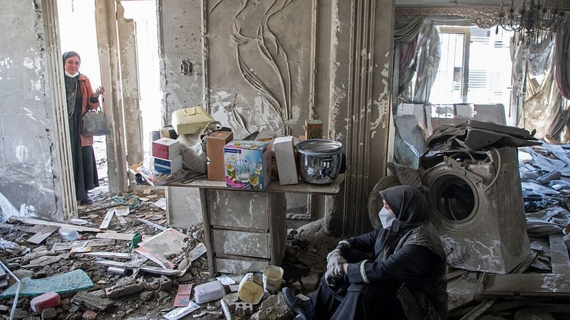 Residents sit amid debris in a residential building that was hit in an airstrike earlier this morning