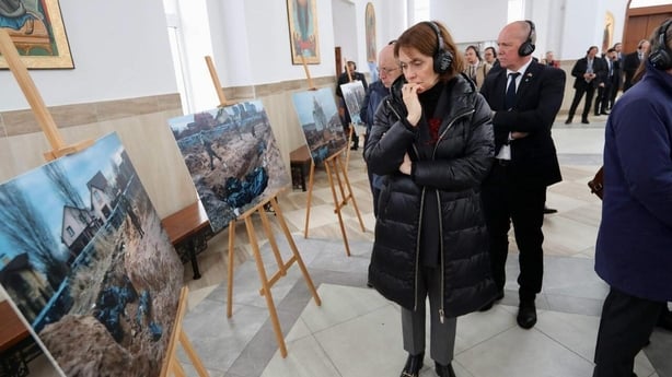 A woman puts her hand to her mouth as she looks at graphic photographs of war destruction