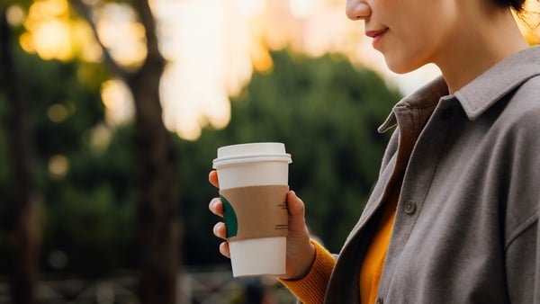 Cropped shot of young Asian woman walking in the park, spending her free time strolling in the nature. Enjoying a carefree and relaxing walk against lush greenery at sunset, drinking a cup of coffee and smiling (Getty Images)