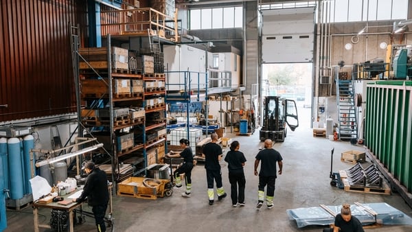 Rear view of male and female warehouse worker in black uniform discussing while walking in manufacturing factory
