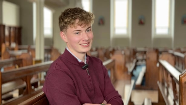 A young man smiles as he sits in a church