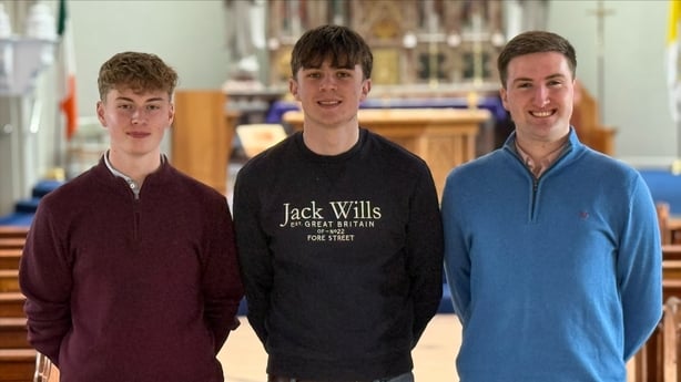 Three young men stand smiling inside a church in Co Carlow