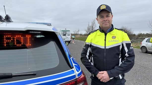 a photograph of inspector adrian queeney standing beside a garda car