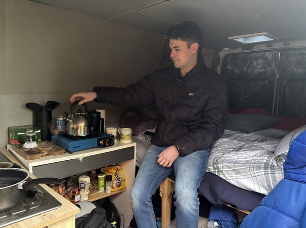 Conor Davidson sitting on his bed in his ban while putting the kettle on a hob