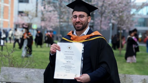 A student named elias amro wearing a cap and gown and holding a degree