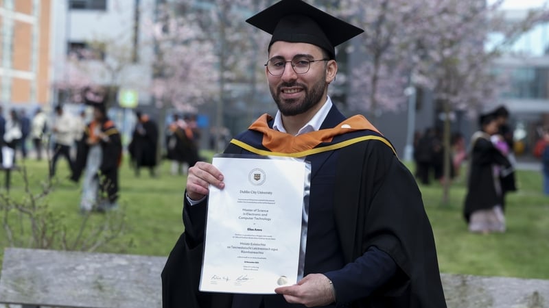 A student named elias amro wearing a cap and gown and holding a degree