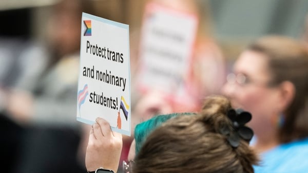 a person holds a sign which reads 'protect trans and nonbinary students'