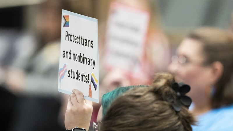 a person holds a sign which reads 'protect trans and nonbinary students'