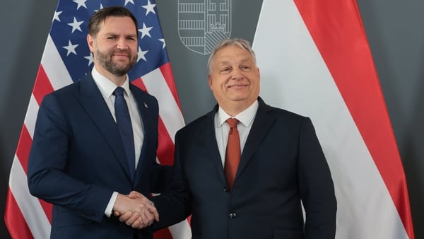 this photograph shows JD Vance shaking hands with Viktor Orban as US and Hungarian flags hang behind them