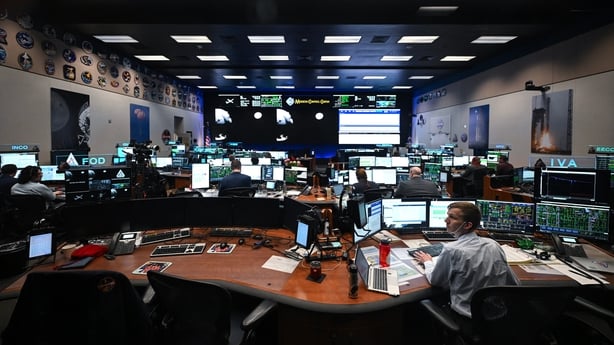 A large room filled with desks and computers screens as people work