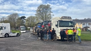 people stand around a lorry with tractors loaded on it