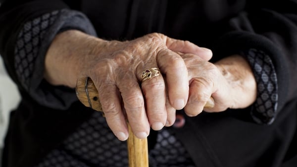 An elderly woman's hands rest gently on a wooden cane