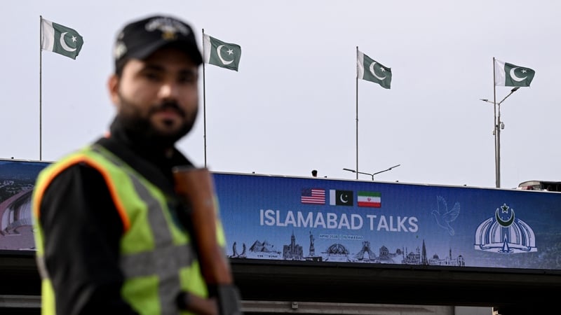 A policeman stands guard in front of a digital screen displaying news of US–Iran peace talks along a road in Islamabad