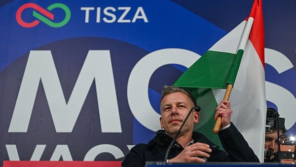 Peter Magyar waves a national flag while standing before a campaign banner