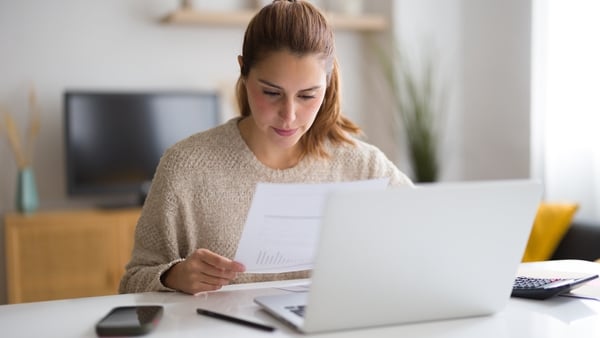 Young woman calculating domestic bills, checking graphs and invoices while working from home
