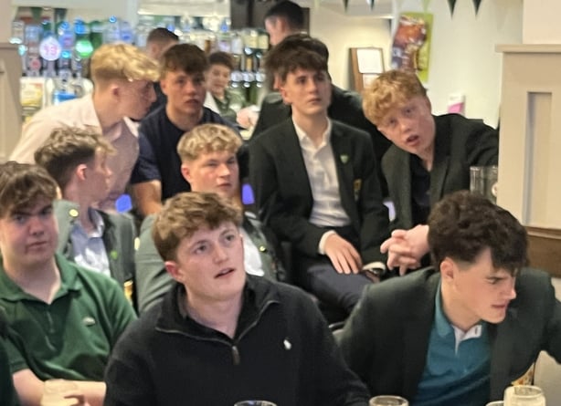 a group of teenage boys watch a television screen showing golf