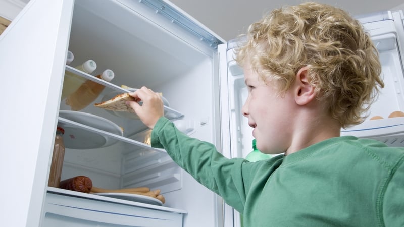 young boy taking a slice of cold leftover pizza from a fridge
