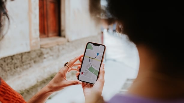 Two woman on vacation use their smart phone, following a map application to their destination.