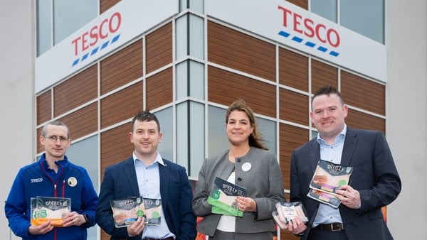 Image of business people holding packets of meats and bacon with a Tesco store in the background