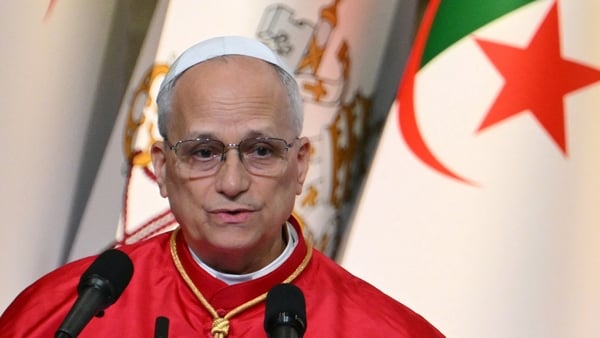Pope Leo standing before Microphones with a two flags behind him