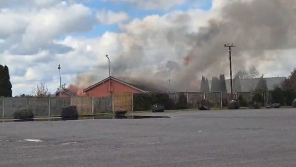 Image shows a red building in the distance with smoke and flames.