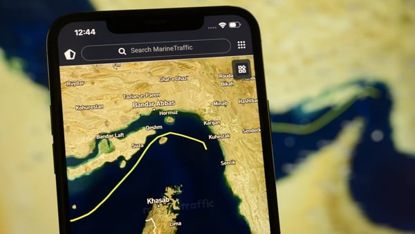 A smartphone displays the MarineTraffic app showing a ship transiting the Strait of Hormuz