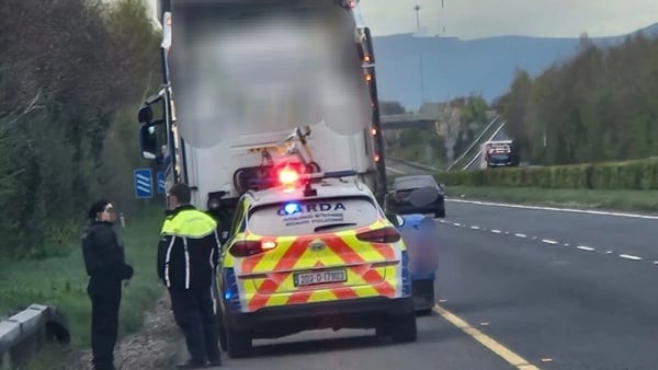 two gardai and a garda car are seen on a hard shoulder of a motorway behind a large trailer