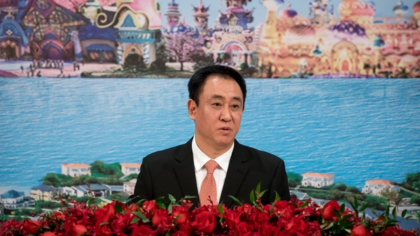 A Chinese businessman sits at a table with a colourful background behind him