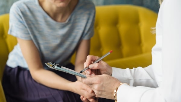 Woman writting to patient girl. Therapist's gestures. Female talks in coworking office. Mother and daughter talk about puberty problems. Top view (Getty Images)