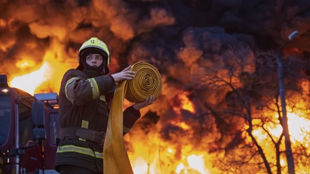 Smoke and flames rise in the background as a firefighter works in Kyiv